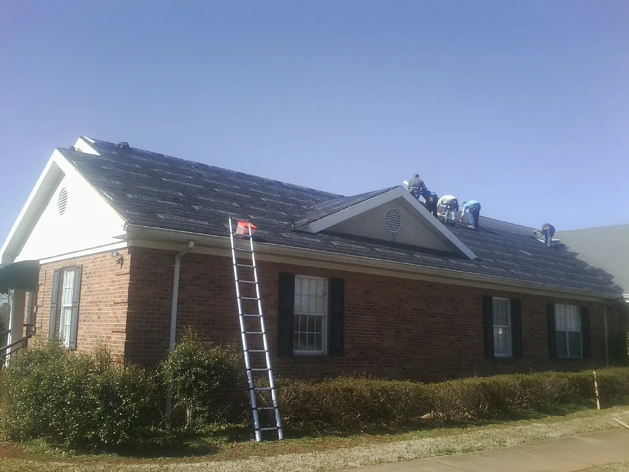 Crew tearing shingles off a brick ranch roof with a ladder set — Metal Roof Repair work by our crew in Bradford